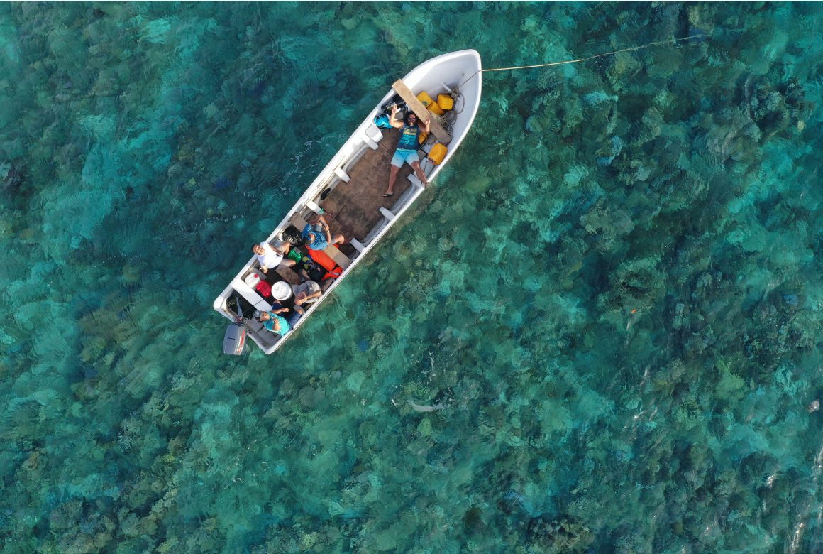 Uma vista de águia com um barco numa massa de água doce. As pessoas no barco estão a olhar para cima com um sinal de paz.
